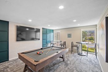 A pool table is in the middle of a room with a chair and a small table.
